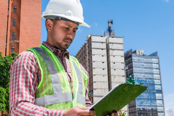 Latin construction worker man looking documents in construction site in sunny day