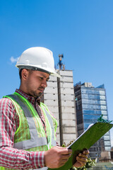 Latin construction worker man looking documents in construction site in sunny day