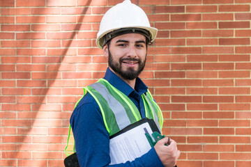 Latin construction worker man holding documents with brick wall at background in sunny day