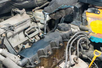 Fototapeta premium Mechanic's hands unscrew the valve cover of an internal combustion engine to replace the gasket