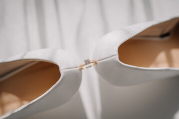 Valmiera, Latvia - July 7, 2023 - Engagement ring balanced between white high-heeled shoes.