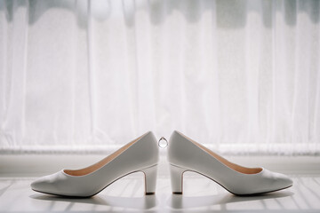 Valmiera, Latvia - July 7, 2023 - Two white bridal shoes are positioned with a wedding ring...