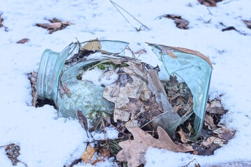 Fototapeta premium one large glass broken jar with brown dry leaves lies in white snow on a winter street