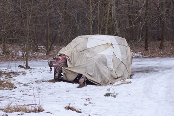 one old dismantled car covered with a gray tarpaulin awning stands in white snow on a winter street