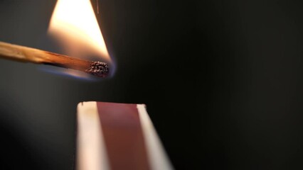 Strikes a match on the side of the box. Smoke and fire appear. The flame ignites. Match lights up. Hands lights a match with a green sulfur head. burns. Super macro shot. Extreme close-up