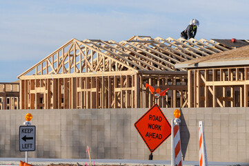 An exterior view of a wooden home under construction, with a worker atop the structure, a block...