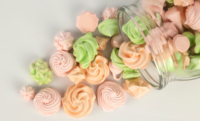 Many colorful meringues pouring out of a glass jar on a white background, close-up, top view