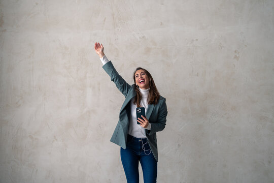 Dancing, Happy Woman Listening To Track, Song Or Audio Podcast On Mobile App In A Studio On Gray Background With Copy Space.