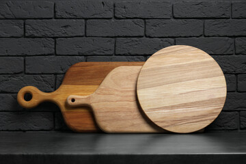 Different wooden cutting boards on gray table near dark brick wall