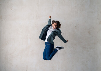 Full length shot of a happy young woman jumping into the air against a gray background. Concept of freedom, celebration, joy.