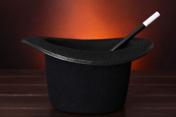 Black top hat and wand on wooden table against color background, closeup. Magician equipment