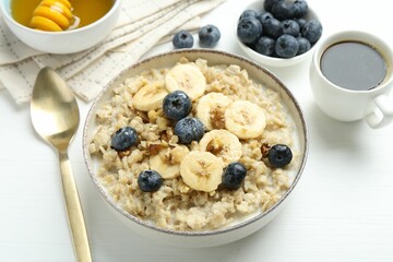 Tasty oatmeal with banana, blueberries, walnuts and honey served in bowl on white wooden table