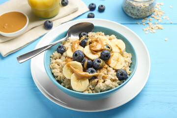 Tasty oatmeal with banana, blueberries and peanut butter served in bowl on light blue wooden table