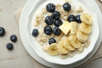Tasty oatmeal with banana, blueberries, butter and milk served in bowl on light grey table, flat lay