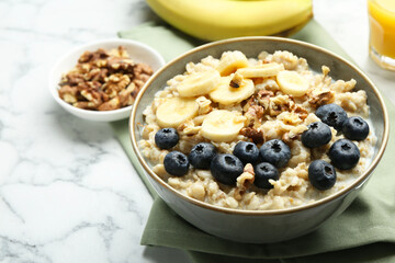 Tasty oatmeal with banana, blueberries, walnuts and milk served in bowl on white marble table, space for text