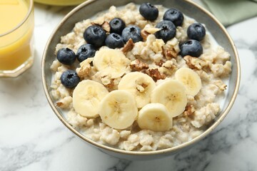 Tasty oatmeal with banana, blueberries, walnuts and milk served in bowl on white marble table, closeup