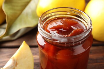 Tasty homemade quince jam in jar and fruits on wooden table, closeup