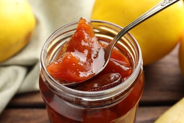 Taking tasty homemade quince jam from jar at table, closeup