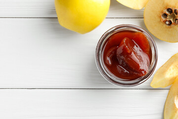 Tasty homemade quince jam in jar and fruits on white wooden table, flat lay. Space for text