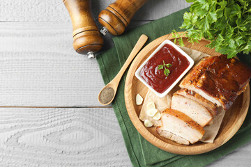 Pieces of baked pork belly served with sauce on grey wooden table, top view. Space for text