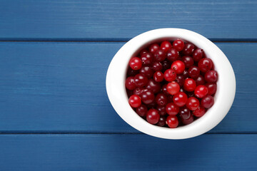 Fresh cranberries in bowl on blue wooden table, top view. Space for text