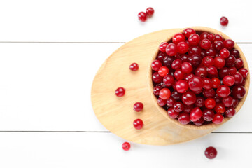 Fresh ripe cranberries in bowl on white wooden table, top view. Space for text