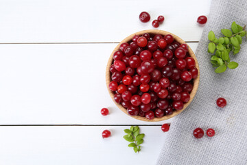 Fresh ripe cranberries and branches on white wooden table, top view. Space for text