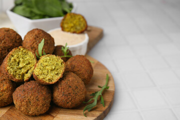 Delicious falafel balls and arugula on white tiled table, space for text