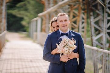 Valmiera, Latvia - July 7, 2023 - A smiling groom in a blue suit holds a bouquet with a bride...
