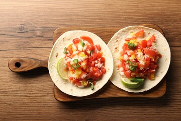 Delicious tacos with vegetables, green onion, lime and ketchup on wooden table, top view