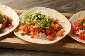 Delicious tacos with vegetables, green onion, lime and ketchup on wooden table, closeup