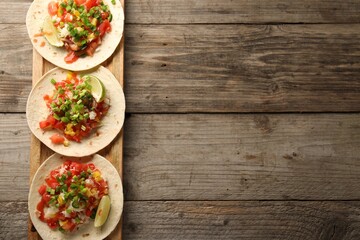 Delicious tacos with vegetables, green onion, lime and ketchup on wooden table, top view. Space for text