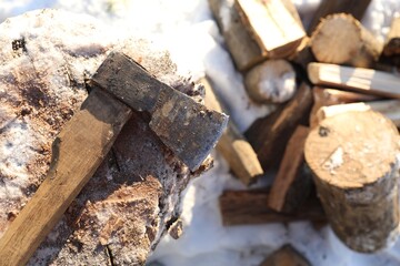 Fototapeta premium Metal axe on wooden log and pile of wood outdoors on sunny winter day, top view. Space for text