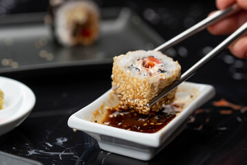 Close up of hands with chopsticks eating japanese food. Traditional asian rolls. Maki sushi with vegetables and tuna