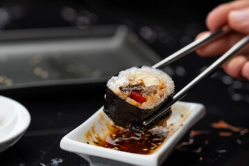 Close up of hands with chopsticks eating japanese food. Traditional asian rolls. Maki sushi with vegetables and tuna
