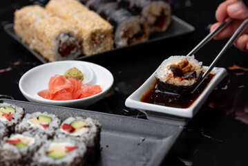 Close up of hands with chopsticks eating japanese food. Traditional asian rolls. Maki sushi with vegetables and tuna
