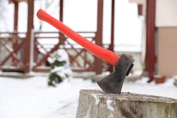 Metal axe in wooden stump outdoors on winter day