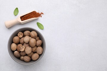 Scoop with nutmeg powder, seeds in bowl and green leaves on light table, flat lay. Space for text