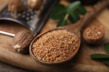 Spoon with grated nutmeg on wooden board, closeup