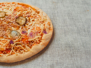 Uncooked burger style Italian pizza with tomato sauce, meat, cucumber and cheese light color table cloth. Ready meals product for cooking home. High quality ingredients