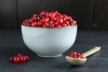 Cranberries in bowl and spoon on black wooden table, closeup