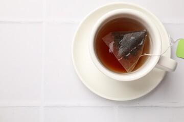 Tea bag in cup with hot drink on white tiled table, top view. Space for text