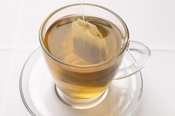 Tea bag in cup with hot drink on white table, closeup