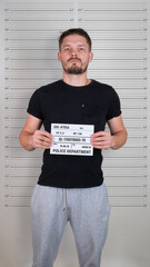 Brunette caucasian man standing with criminal mugshot letter board at police department