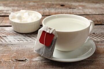 Tea bag and cup with hot water on wooden rustic table, closeup