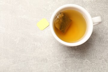 Brewing tea. Cup with tea bag on light table, top view. Space for text