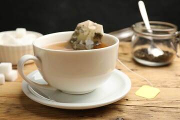 Tea brewing. White cup with tea bag on wooden table, closeup