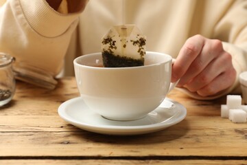Tea brewing. Woman putting tea bag into cup at wooden table, closeup