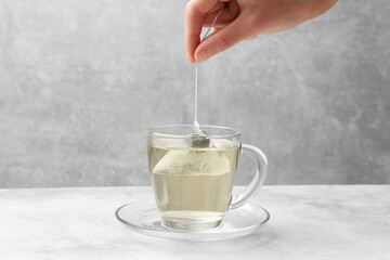 Tea brewing. Woman putting tea bag into cup at light table, closeup