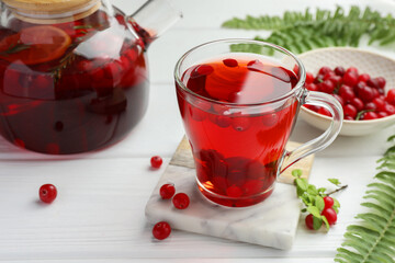 Tasty hot cranberry tea in glass cup, fresh berries and leaves on white wooden table